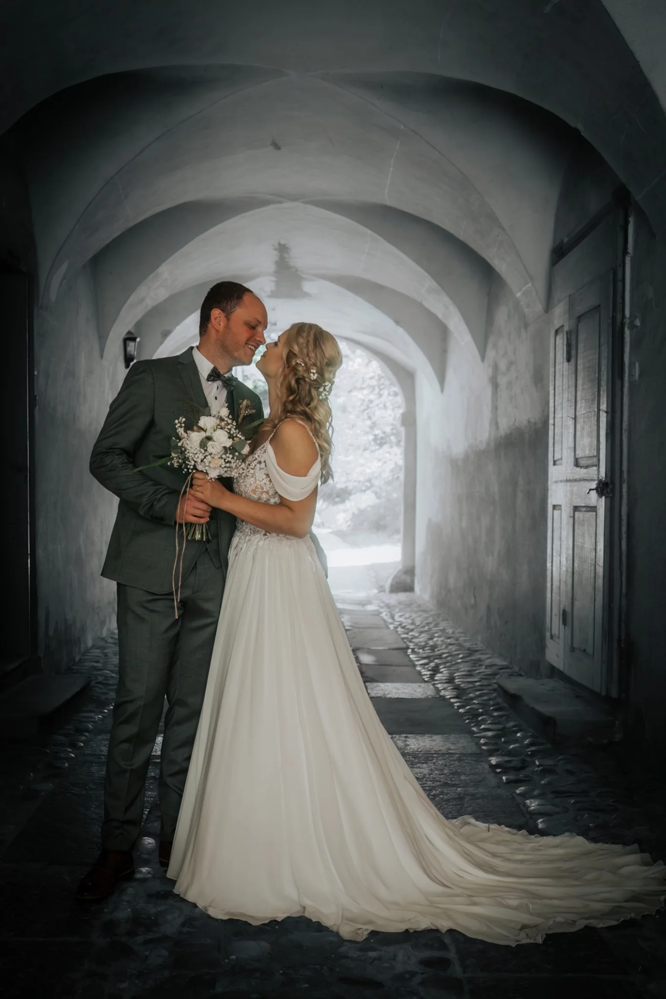 Brautpaar umarmt sich unter einem historischen Steinbogen – romantisches Hochzeitsportrait
