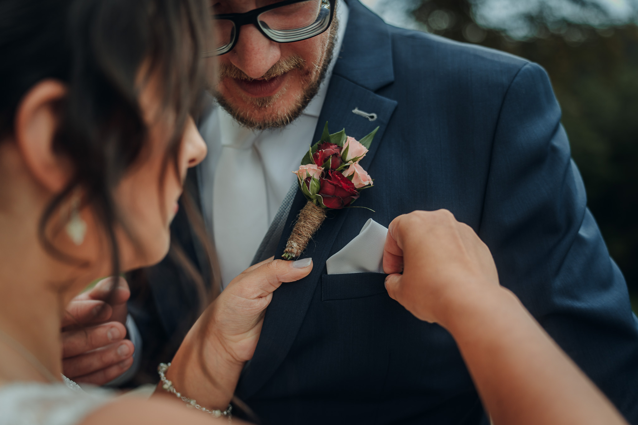 Ein Hochzeitsanstecker wird am Jackett des Bräutigams befestigt.